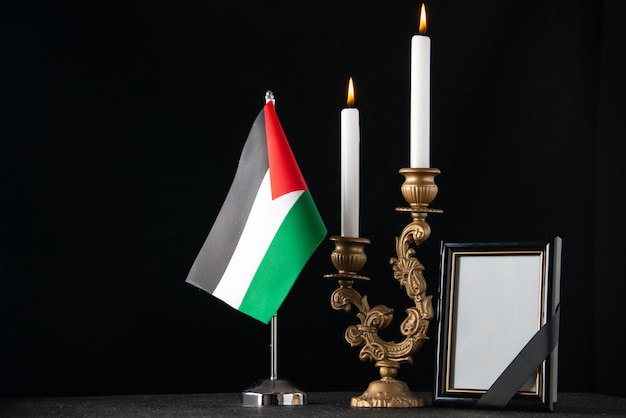 Front view burning candles with palestinian flag and picture frame dark surface