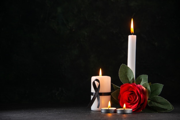 Front view of burning candles with red flower on dark surface