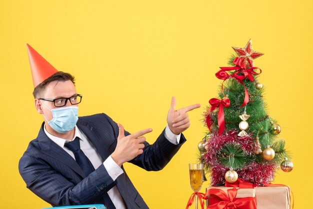 Front view of business man pointing at xmas tree and presents on yellow