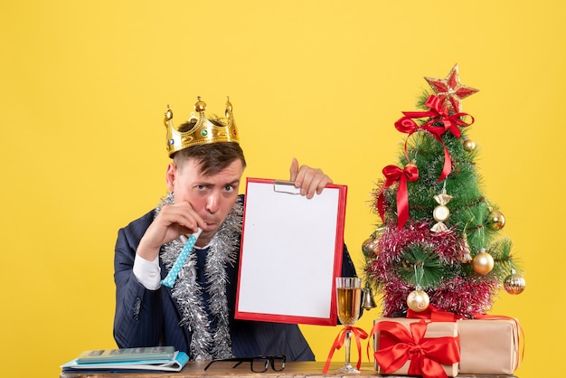 크리스마스 트리 근처 테이블에 앉아 소음기를 사용하여 비즈니스 남자의 전면보기 및 노란색 선물