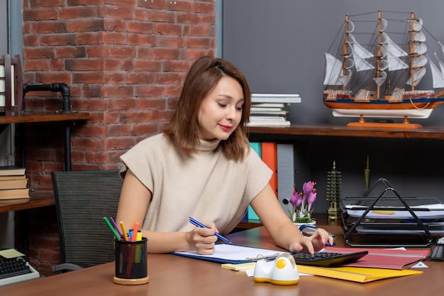 Front view business woman using calculator sitting at desk in office