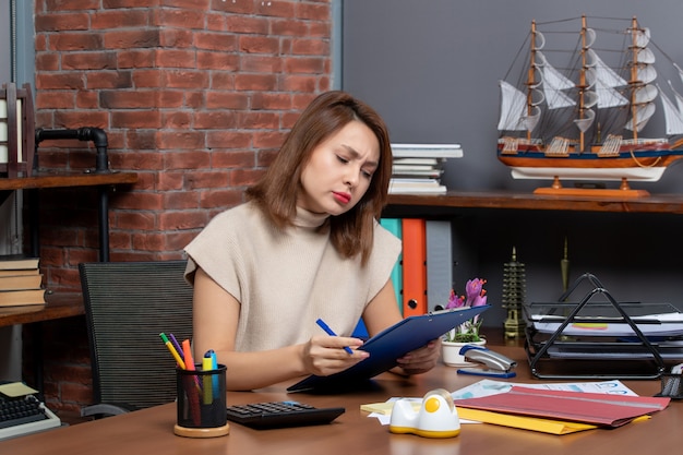 Front view busy business woman checking documents sitting at desk in office