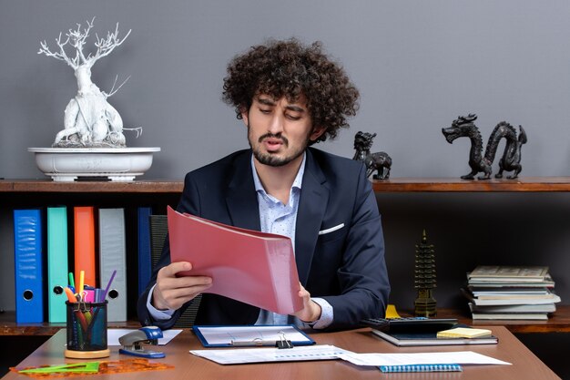 Front view busy businessman sitting at the desk holding files in his office