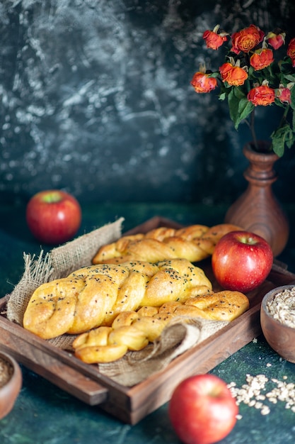 Front view cable-knit breadsticks on rectangle wood board apples flowers in vase on table