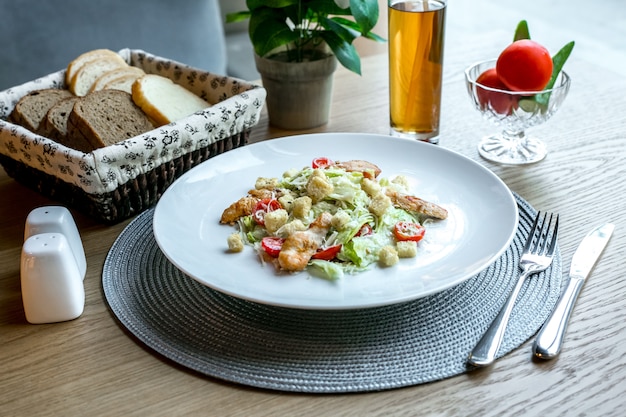 Вид спереди салат Цезарь с курицей на тарелке с ломтиками белого и черного хлеба и с безалкогольным напитком на столе