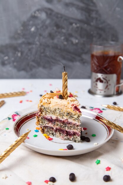 Вид спереди кусочка торта внутри тарелки со свечным чаем и маленькими звездными знаками на светлой поверхности