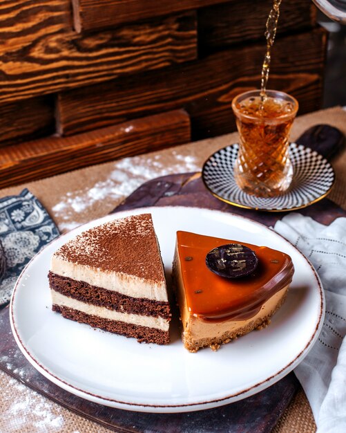 Front view cake slices chocolate cake pieces inside white plate along with hot tea on the brown floor