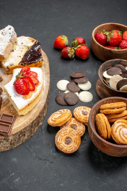 Foto gratuita fette di torta vista frontale con barrette di cioccolato e biscotti su sfondo grigio