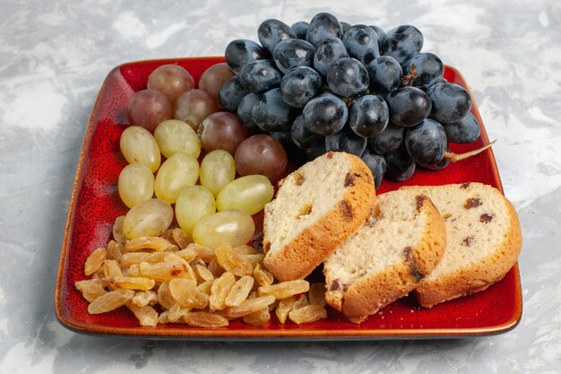 Free photo front view cake slices with grapes and raisins inside red plate on white surface