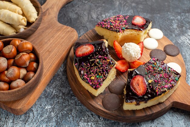 Front view cake slices with nuts and sweets on dark background