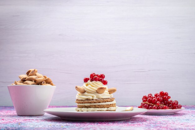 Front view of cake with cream along with cookies and cranberries on the light surface