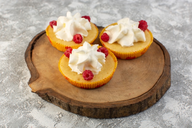 Front view of cakes with cream yummy baked designed with raspberry on the wooden desk