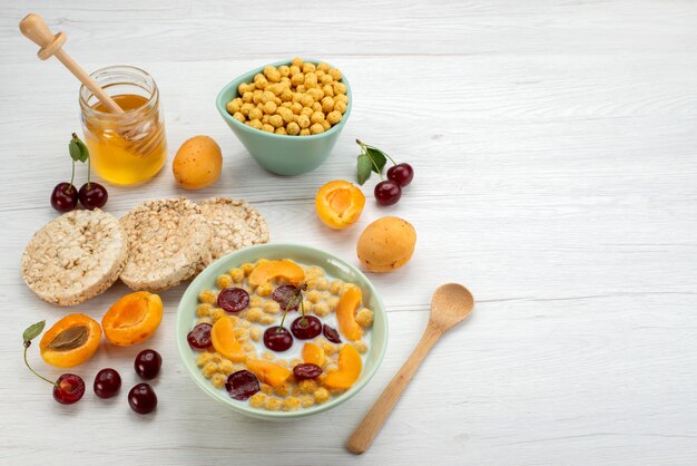 Front view cereals with milk inside blue plate with crackers fruits and honey on the white desk drink milk dairy creamery breakfast