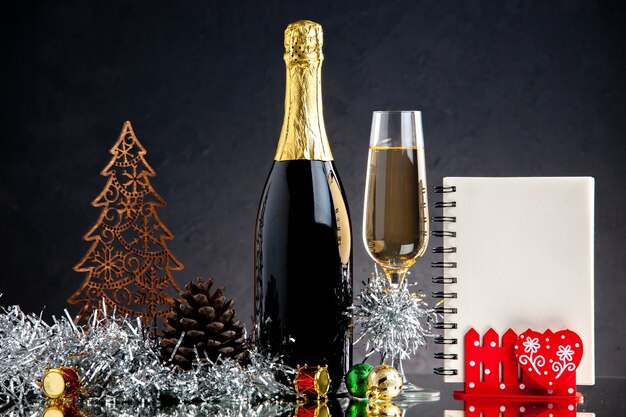Стеклянная бутылка шампанского, вид спереди, рождественские украшения для ноутбука на темной поверхности
