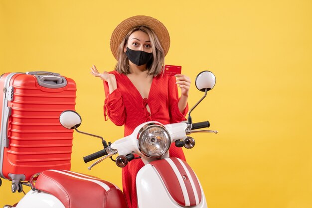 Front view of charming woman with black mask holding discount card near moped