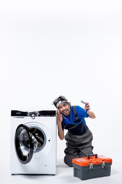 Free photo front view cheerful repairman holding stethoscope sitting near washer on white space