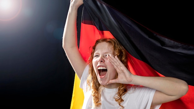 Вид спереди ликующей женщины, держащей немецкий флаг