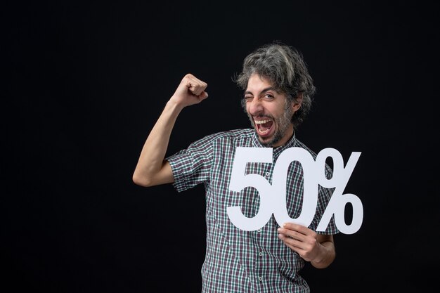 Front view cheery man with winner expression holding up mark on dark wall