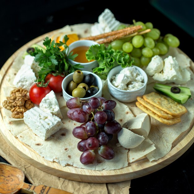 Front view cheese plate on pita bread with grapes olives honey and tomatoes