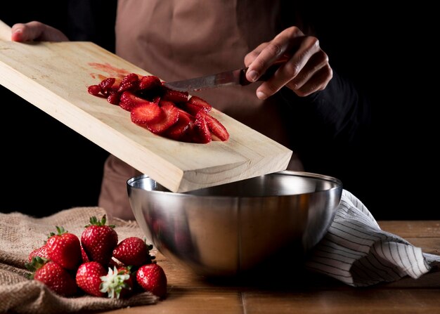 Front view of chef adding chopped strawberries in bowl