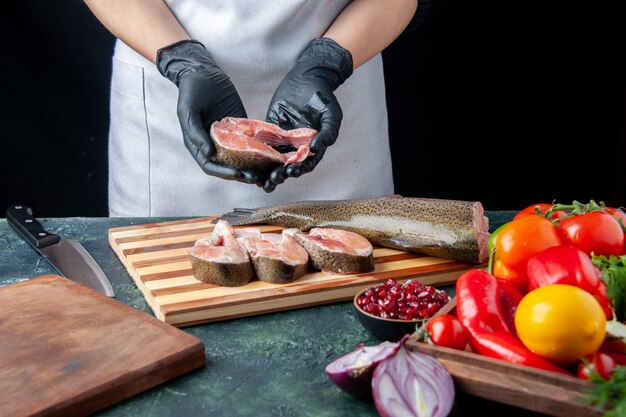 앞치마를 입은 앞치마 요리사가 식탁에 있는 나무 서빙 보드 칼에 생선 조각 야채를 들고 있다