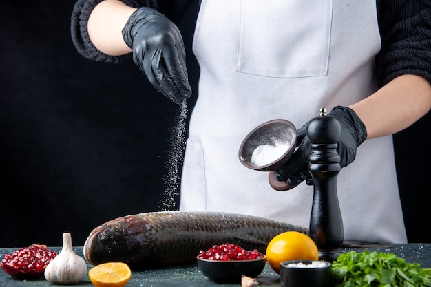 앞치마를 입은 주방장이 식탁에 있는 그릇에 있는 신선한 생선 석류 씨앗에 소금을 뿌렸다
