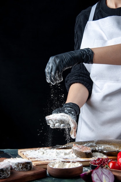 Front view chef covering raw fish slices with flour on kitchen table on black surface