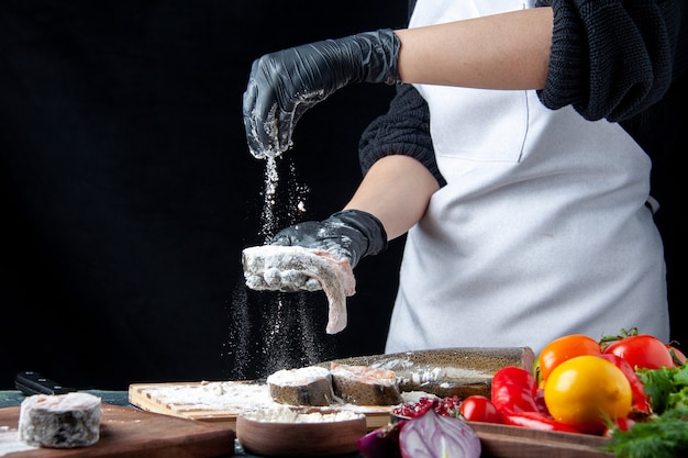 Front view chef covering raw fish with flour fresh vegetables on wood board flour bowl on kitchen table