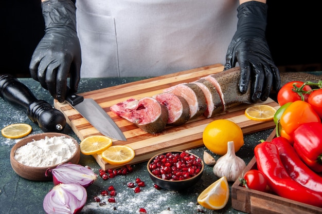 Front view chef holding raw fish slices and knife on cutting board vegetables on wood serving board on kitchen table