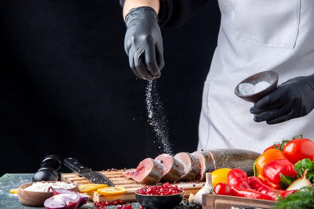 Front view chef sprinkled flour on raw fish slices on cutting board vegetables on wood serving board knife on kitchen table