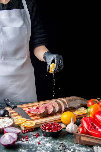 Вид спереди шеф-повар сжимает лимон на нож для ломтиков сырой рыбы на разделочной доске на кухонном столе