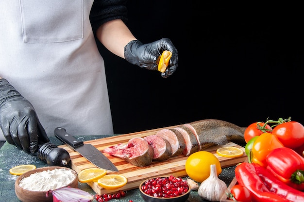 Front view chef squeezing lemon on raw fish slices knife on cutting board vegetables on wood serving board