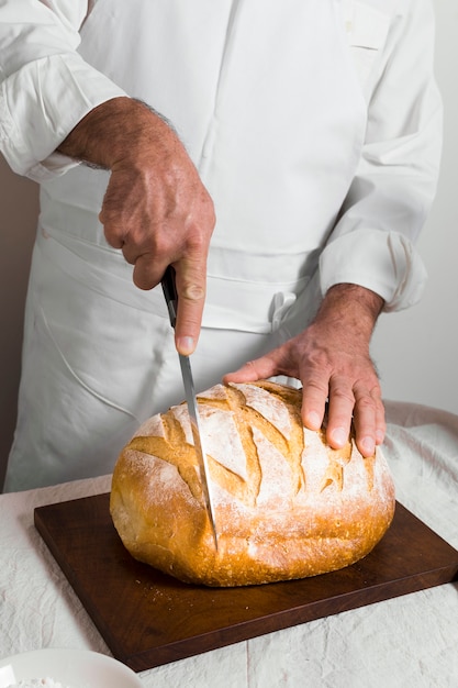 Front view chef wearing white clothes cutting a bread