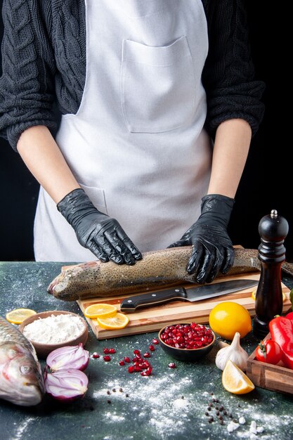 Front view chef in white apron chopping raw fish on wood board pepper grinder flour bowl pomegranate seeds in bowl on kitchen table