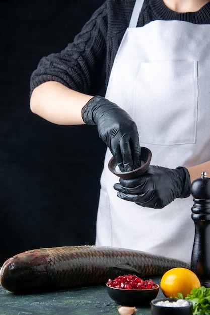 Front view chef in white apron sprinkled salt onto fresh fish pomegranate seeds in bowl pepper grinder on table