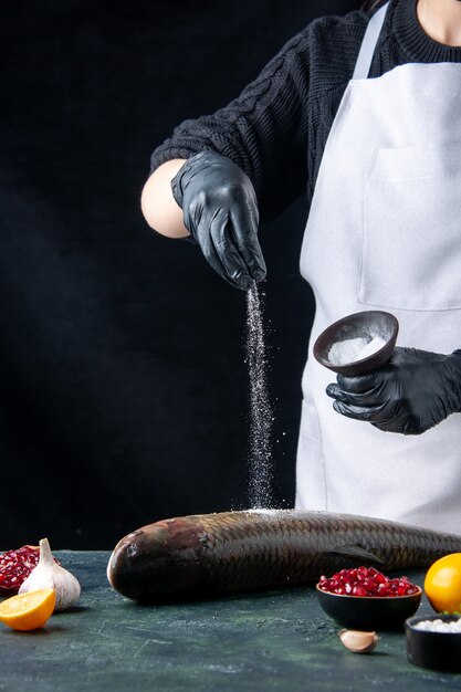 Front view chef in white apron sprinkled salt onto fresh fish pomegranate seeds in bowl on table