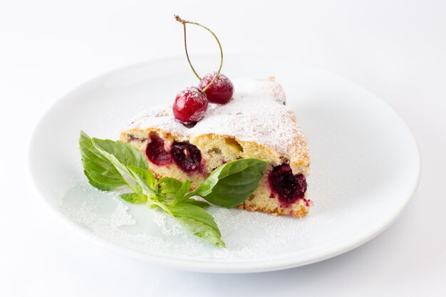 Front view of cherry cake slice inside white plate with sugar powder on the white desk