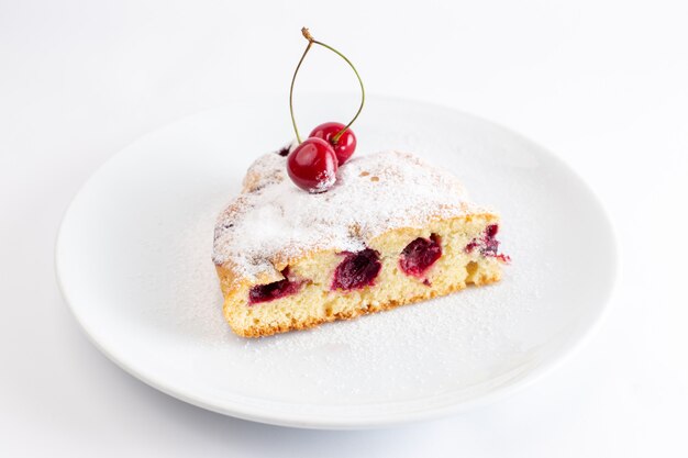 Front view of cherry cake slice inside white plate with sugar powder on the white surface