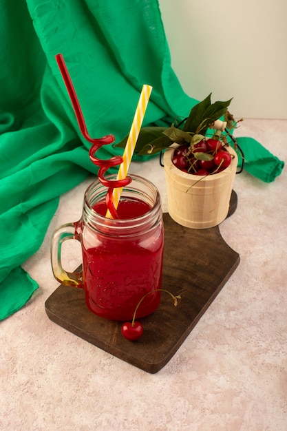 Foto gratuita un cocktail rosso ciliegia con vista frontale con cannucce all'interno di un piccolo barattolo di raffreddamento fresco sulla scrivania in legno insieme a ciliegie fresche sul rosa