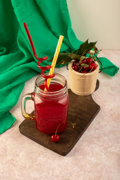 Красный вишневый коктейль, вид спереди, с соломкой внутри маленькой банки, свежее охлаждение на деревянном столе вместе со свежей вишней на розовом