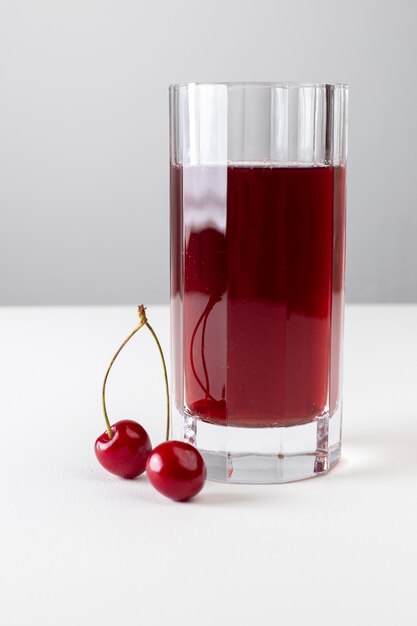 Front view of cherry juice inside long glass on the white surfac