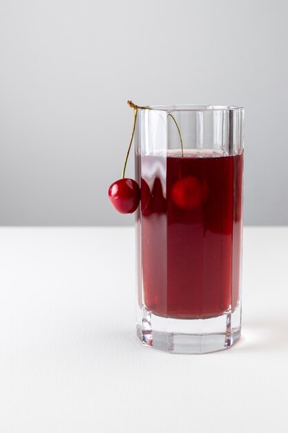 Front view of cherry juice inside long glass on the white surface