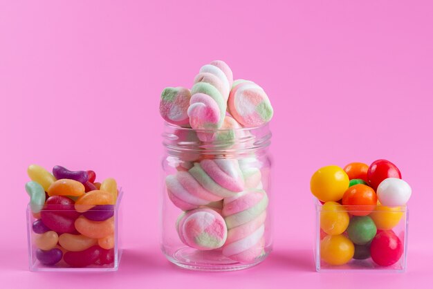 A front view chewing marshmallows along with colorful marmalades and candies on pink, candy color sweet
