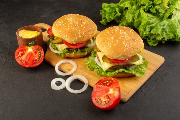 A front view chicken burger with cheese tomatoes and green salad on the wooden desk and sandwich fast-food meal