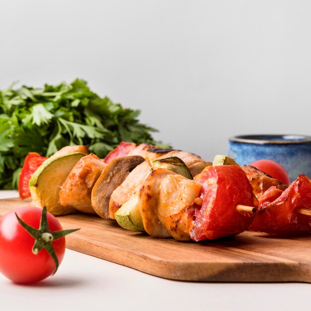 Front view chicken skewers on cutting board with tomato