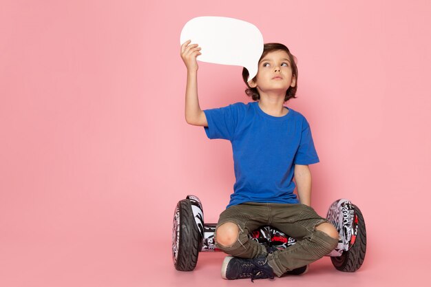 ピンクの床のセグウェイに座っている青いtシャツで愛らしい甘い正面の子少年