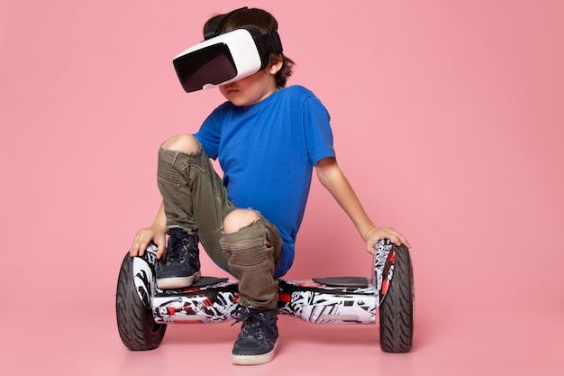 a front view child boy in blue t-shirt and khaki trousers riding segway on the pink floor