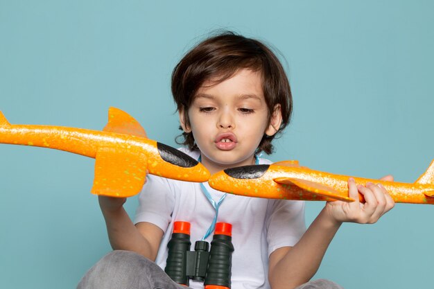 front view child boy cute adorable playing with toy orange planes on blue