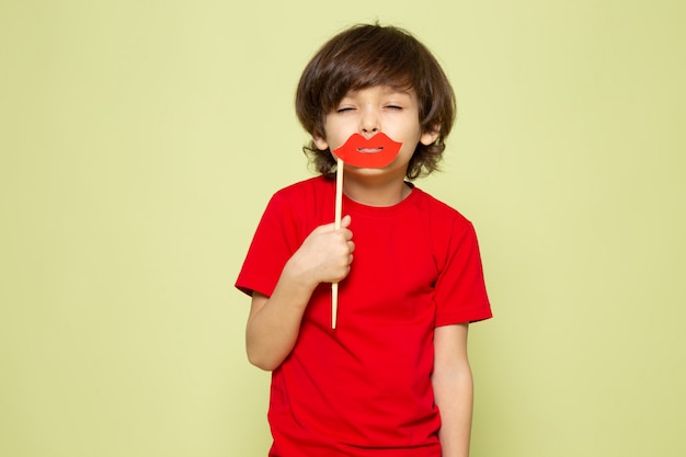 A front view child boy in red t-shirt holding lips stick on the stone colored space