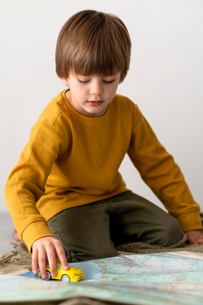 Вид спереди ребенка, играющего с игрушечной машинкой на карте